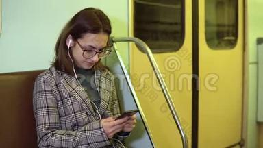 一个<strong>年轻</strong>的女人用耳机听音乐，她手里拿着一部手机在地铁<strong>火车上</strong>。 这个女孩正在写信